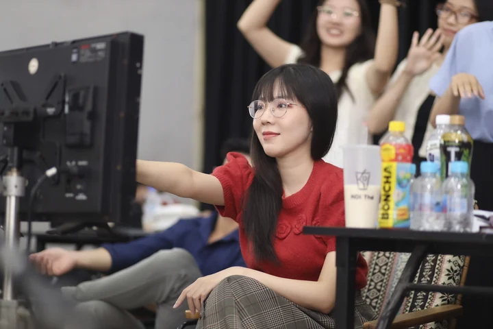 Christy seated and reaching towards a production monitor, with people and props behind her